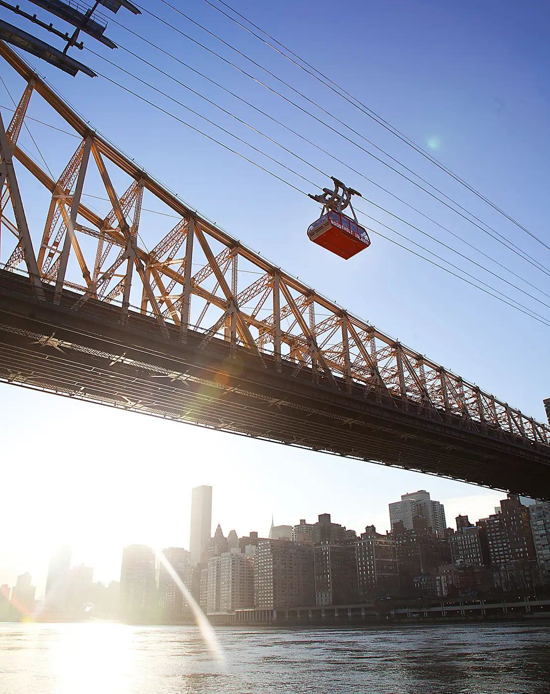Leitner-Poma’s Roosevelt Island Tram glides above the East River beside the Queensboro Bridge in New York City, carrying passengers with the Manhattan skyline in the background.