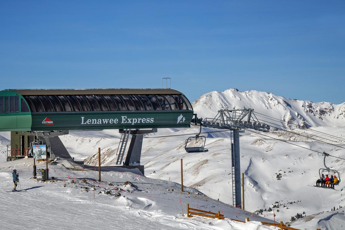 Leitner-Poma Lenawee Express chairlift at Arapahoe Basin with terminal station and chairs in operation against a snowy high-alpine mountain landscape in Colorado.